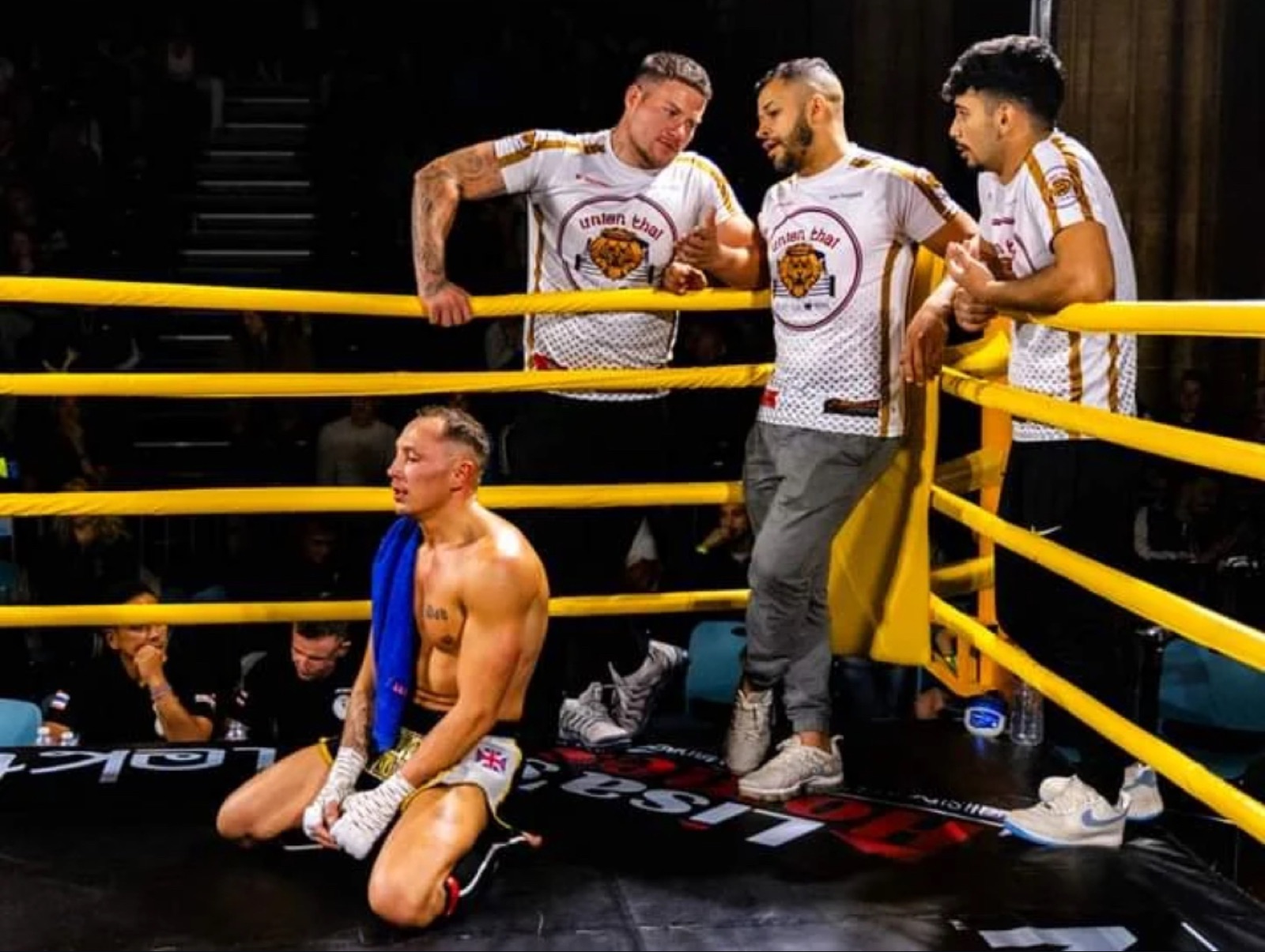 Union Thai cornermen in team shirts coaching a fighter between rounds