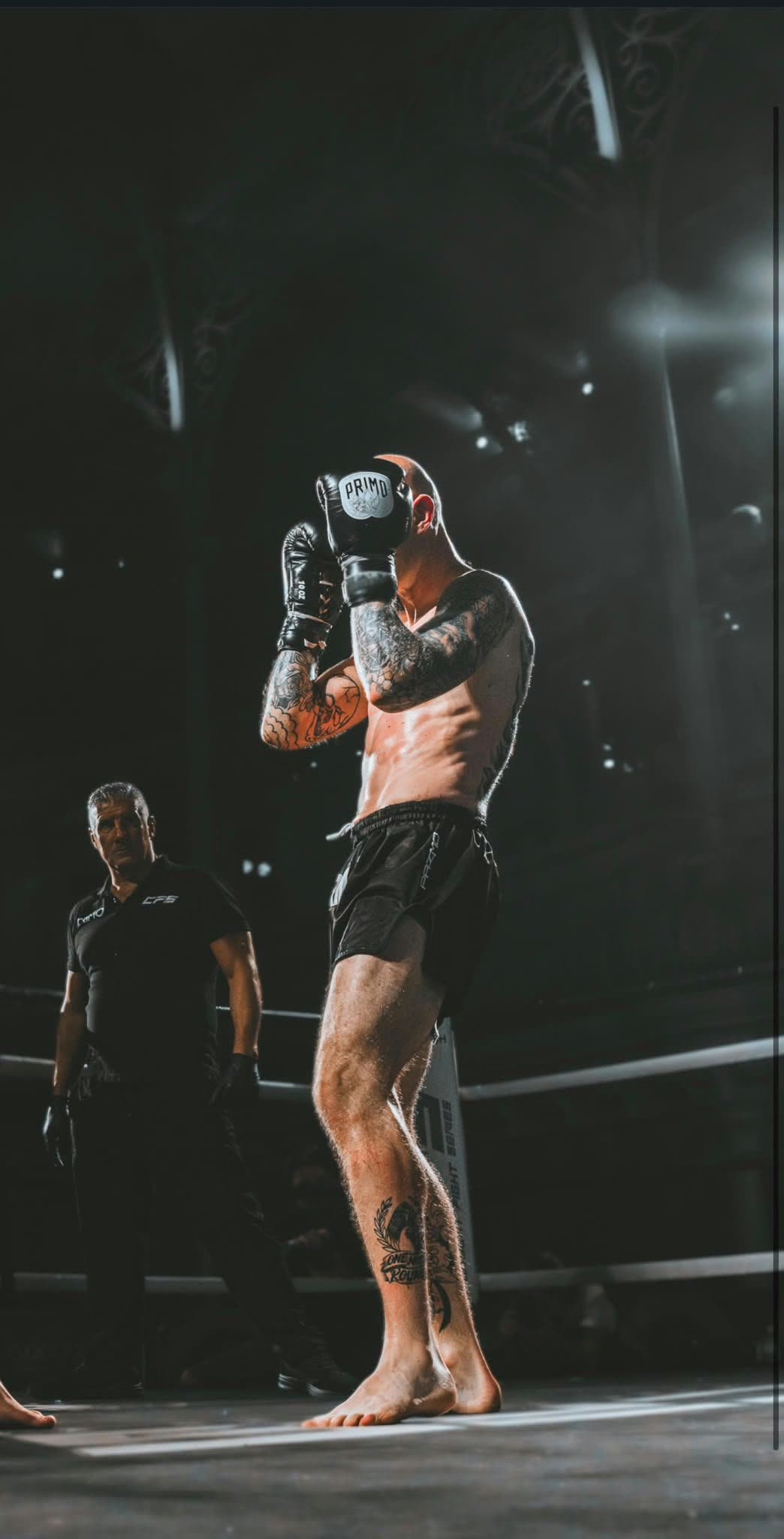 Tattooed fighter with gloves raised under the ring spotlight